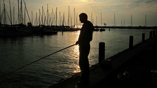 Telihold okozta ezüsthíd a Balatonnál, horgász sziluettjével.